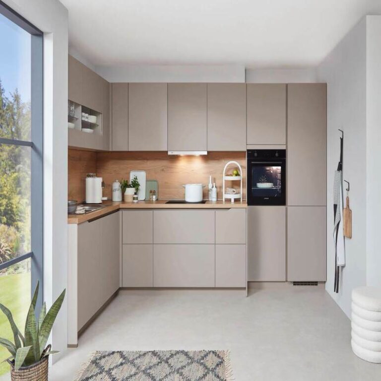 Musterküche in Kaschmir als L-Küche mit Holzrückwand und Backofen im Hochschrank